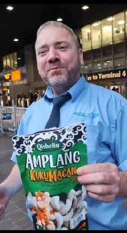 A customer at an airport showing a pack of Qisbelin Amplang Kuku Macan