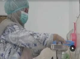 Production staff in mask and hairnet operating a machine